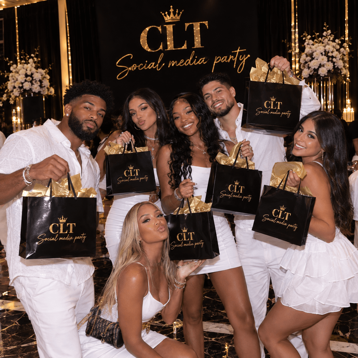 Six people in white outfits holding black gift bags at a CLT Social media party.